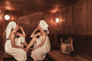 Russian bathhouse. Two women relaxing and sweating in wooden sauna with hot steam. Females with bath